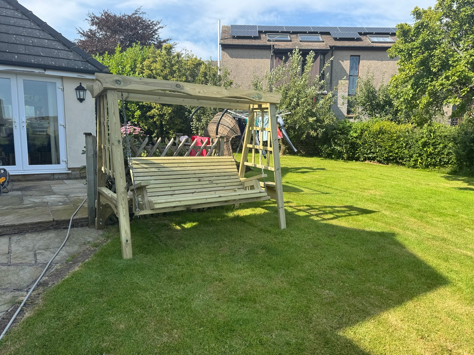 Lilly 3 seat wooden garden swing shown in a real garden setting